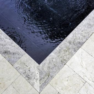 Close-up view of the corner of a tiled stone luxury pool edge with water gently rippling inside the pool.
