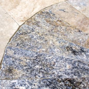 Close-up of stone tiles arranged in a curved pattern, featuring both rough-textured and smooth surfaces in various shades of beige and gray—perfect for enhancing outdoor living spaces or complementing inground pools.