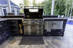 Outdoor kitchens shine with this stainless steel grill station featuring storage drawers, a closed dishwasher, and granite countertop—perfect for outdoor living beside the pool, trees, and even custom spas.