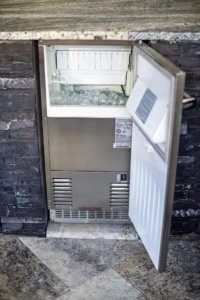 A stainless steel under-counter ice maker with its door open, showing ice cubes inside the compartment—perfect for luxury pools and outdoor living spaces.