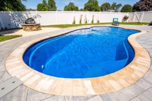 Backyard with a kidney-shaped luxury pool, surrounding stone patio, white privacy fence, a fire pit, lounge chair, and space for outdoor kitchens.