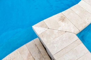 Close-up view of a light-colored stone edge and corner beside a bright blue luxury pool, perfect for elegant outdoor kitchens and relaxing custom spas.