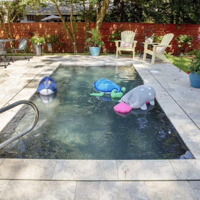 Small backyard pool with three large inflatable animal toys, surrounded by a stone deck, patio furniture, and potted plants—perfect for outdoor living and relaxing by the water.