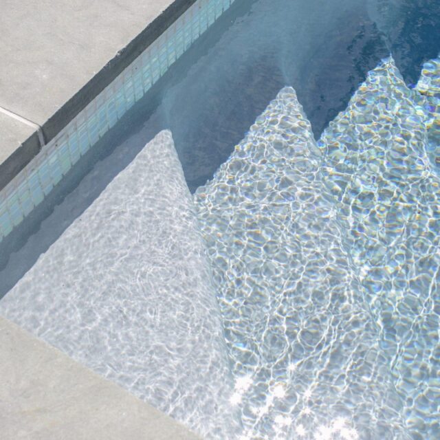 Close-up view of swimming pool steps submerged under clear water, with sunlight creating shimmering patterns on the pool floor—an inviting scene often found alongside custom spas and fiberglass pools.