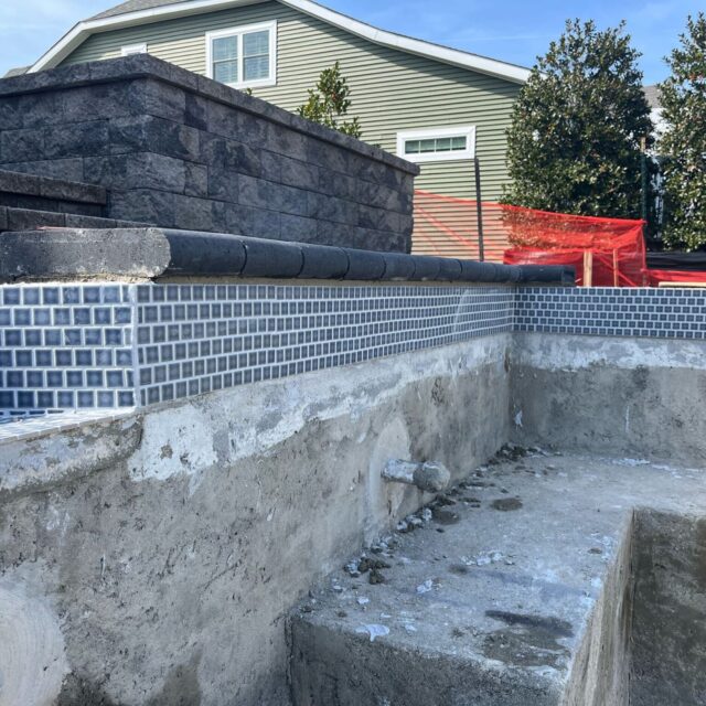 Partially constructed inground pool with exposed concrete, installed tile border, and unfinished walls in a residential backyard—a glimpse of future luxury pools and outdoor living.