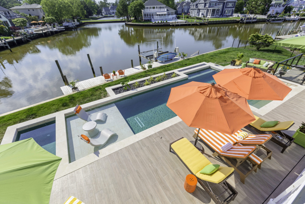 luxury swimming pool with tanning ledge, fire feature and beautiful patio with orange umbrellas and chaise loungers