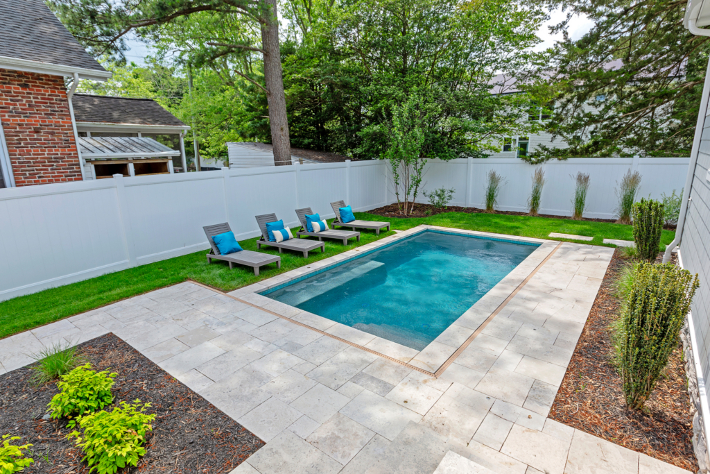 Photo of custom concrete pool with pool chairs around, white privacy fence and restored from pool construction with landscaping