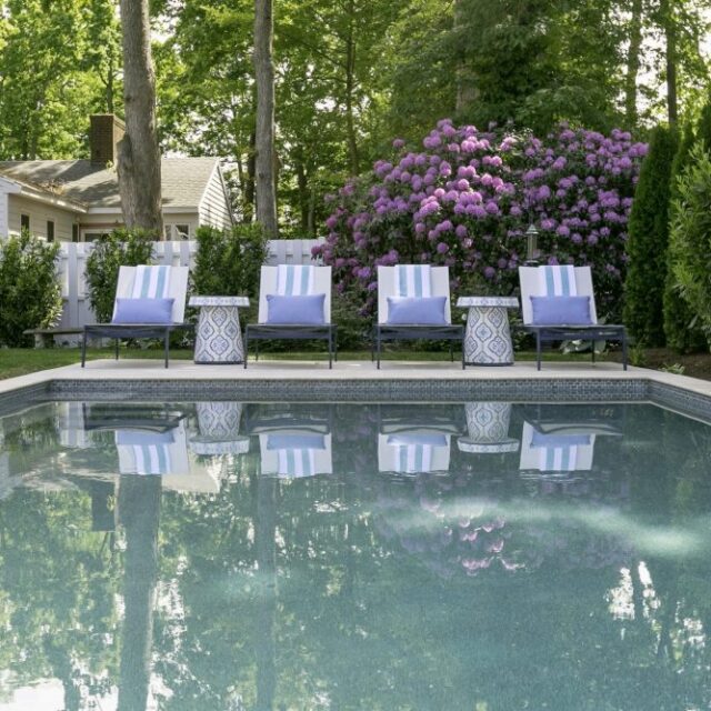 Four striped lounge chairs line the edge of a luxury pool, with flowering bushes and trees in the background.