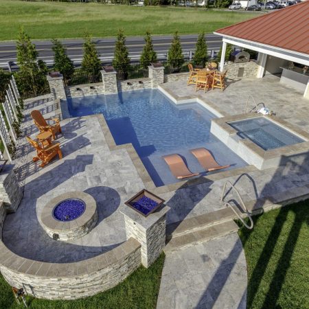 Aerial view of a backyard with an inground swimming pool, hot tub, lounge chairs, fire pit, outdoor living space, and a yellow slide near a grassy yard.