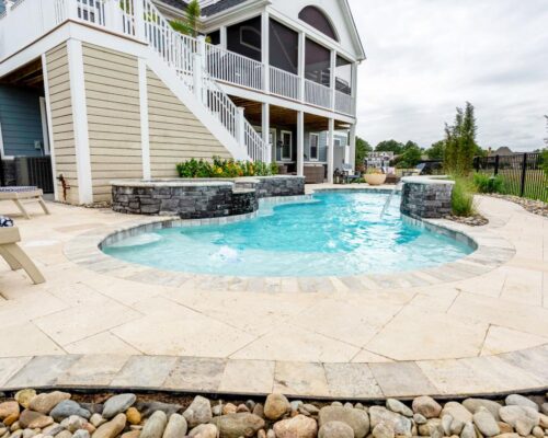 Backyard view of a modern house with a small fiberglass pool, stone patio, lounge chairs, landscaped rocks, and a staircase leading to a screened porch.