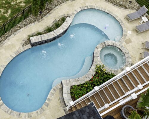 Aerial view of a backyard featuring a luxury pool in a kidney shape with attached spa, two lounge chairs, and a wooden deck bordered by landscaping, perfect for elevated outdoor living.
