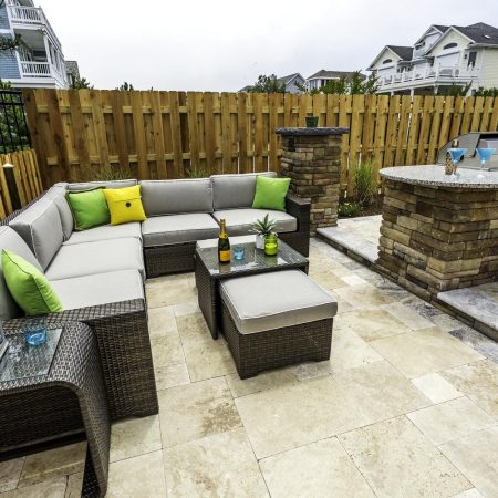 Outdoor patio featuring a wicker sectional sofa, colorful cushions, and a coffee table pairs perfectly with outdoor kitchens and a built-in grill, all surrounded by a wooden fence and nearby houses.