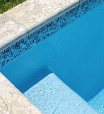 A close-up view of a luxury pool corner with blue water, tiled edges, a submerged step, and grass visible at the top left—perfectly complementing custom spas or outdoor kitchens in your backyard oasis.