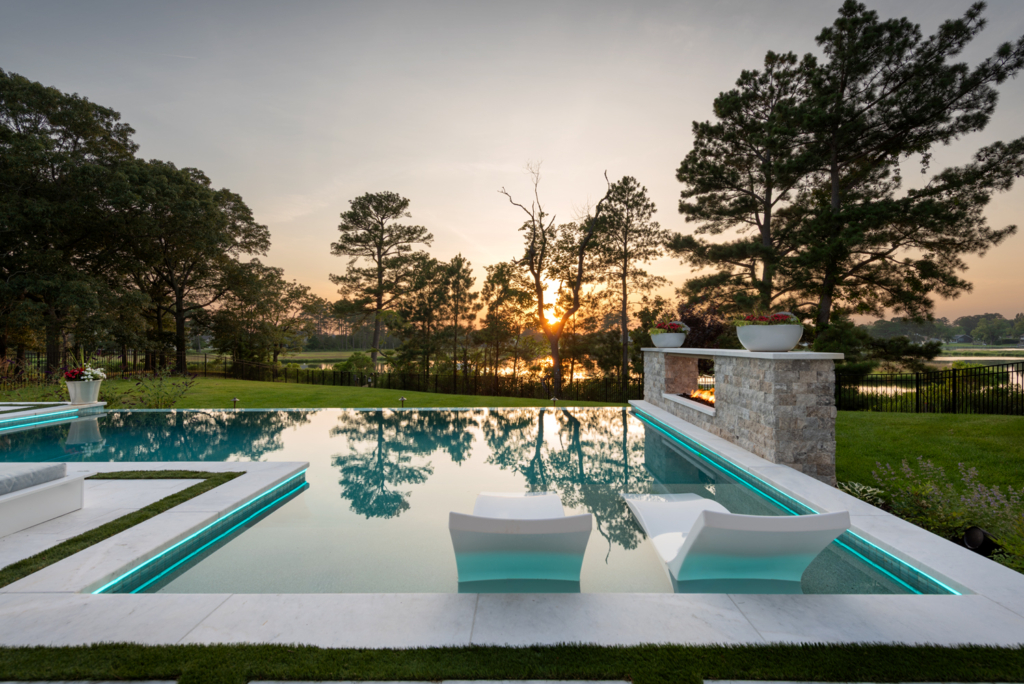 Sunset photo of luxury pool with an infinity edge, built in fire pit with ledge seating