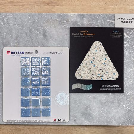 A sample board displays blue glass tiles, a triangular aggregate sample labeled White Diamonds, and a gray marble slab labeled Afyon Cloud Antiqued—perfect accents for inground pools or stylish outdoor kitchens.