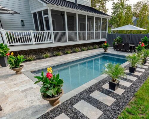 Rectangular backyard fiberglass pool with stone patio, potted plants, stepping stones, outdoor dining set, and a screened porch attached to a gray house—perfect for relaxed outdoor living.
