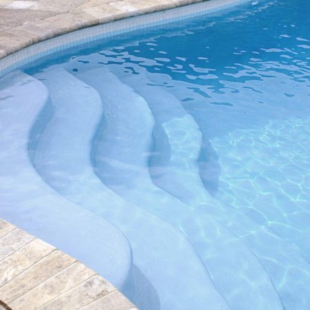 Curved stone steps lead into a clear blue inground pool, with gentle ripples on the water’s surface—perfect for those who appreciate luxury pools and relaxing retreats.