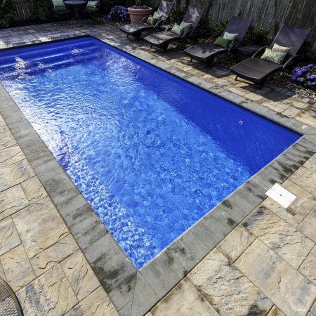 Rectangular in-ground fiberglass pool surrounded by stone tile patio, with several lounge chairs and potted plants along the fence—perfect for enjoying the comfort of luxury pools.