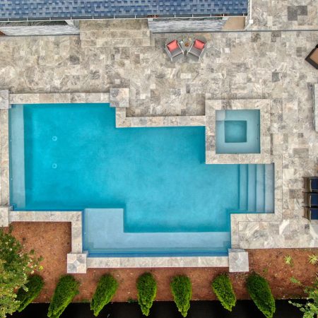 Aerial view of a backyard with a rectangular inground pool, hot tub, lounge chairs, dining table, fire pit seating, outdoor kitchens, and surrounding landscaping—perfect for outdoor living.