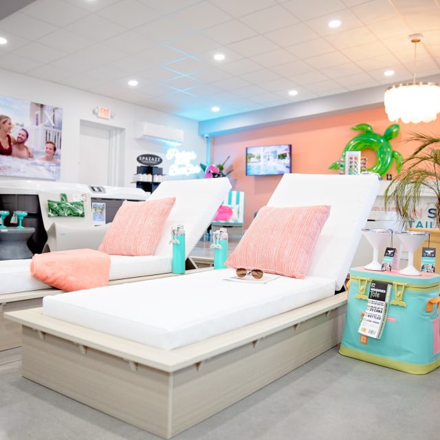 Two white lounge chairs with pink cushions and beach accessories are displayed in a bright, modern showroom with a tropical theme, perfect for enhancing your outdoor living space or relaxing by luxury pools.