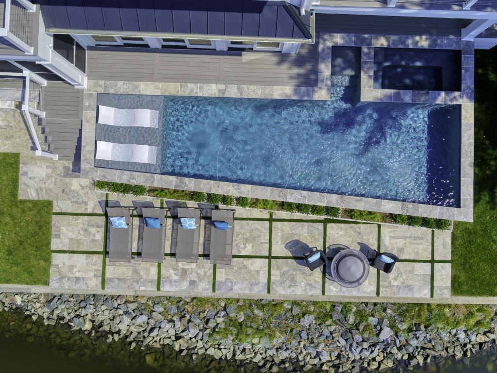 Aerial photography of a luxury pool that is raised with a beautiful patio with turf inlay and ledge lounger furniture on the tanning ledge of the pool