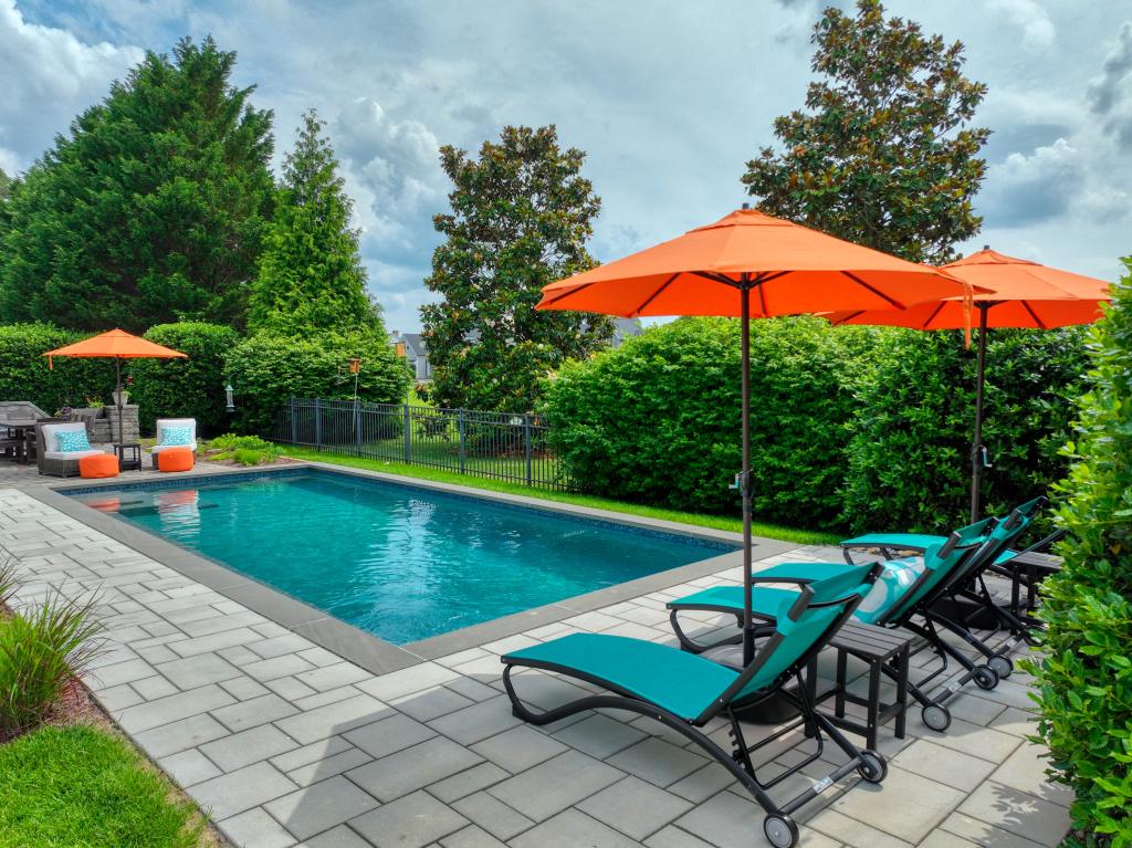 photography of a backyard with a gunite pool and patio around, with turquois lounge chairs with orange umbrellas