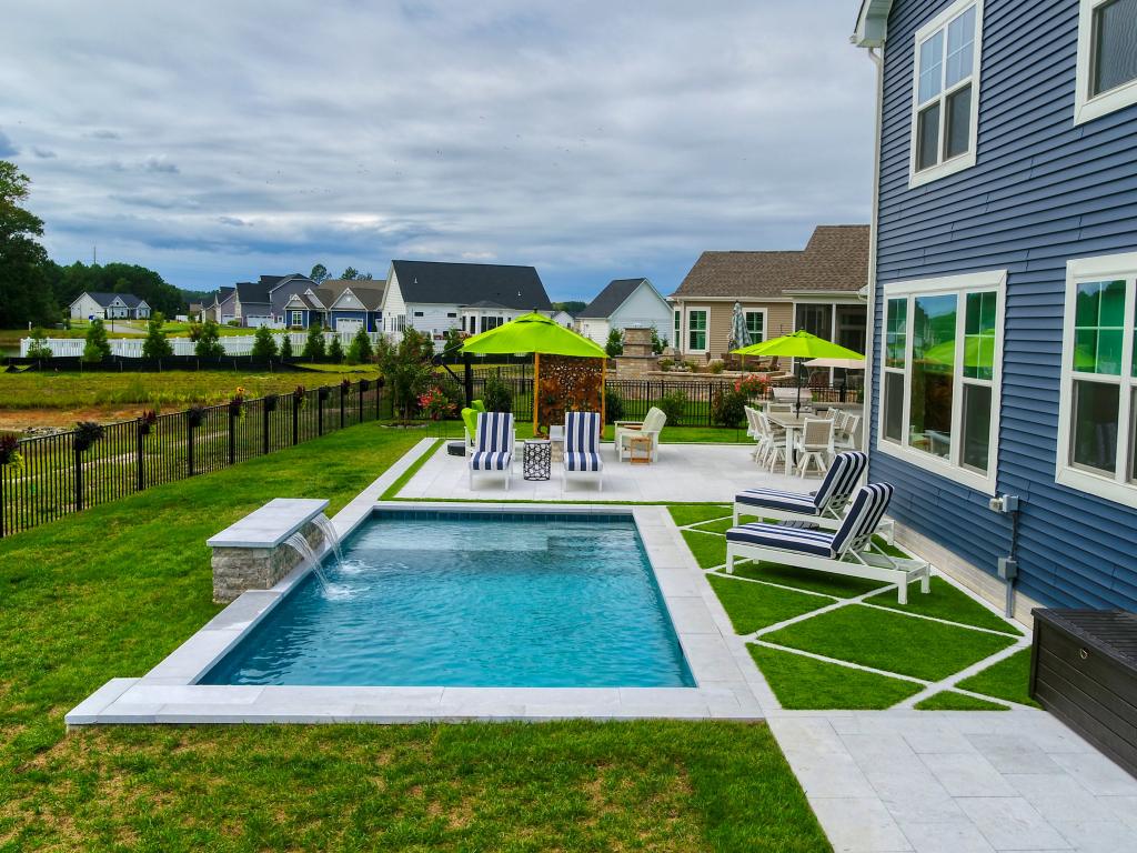 Photograph of custom pool with water feature, patio, and turf inlay, green pool umbrellas, along with lounge chairs with blue and white stripe cushions